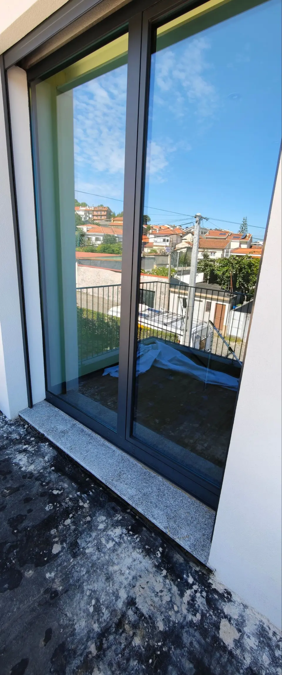 Janela de correr com restos de obra no parapeito de pedra, antes da limpeza